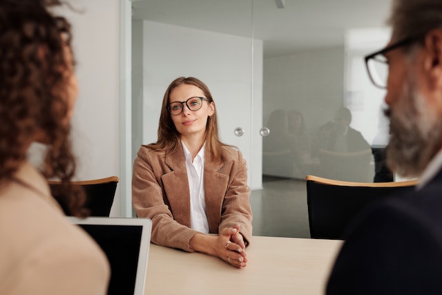 person in a brown suit and black glasses speaking with two managers in a conference room